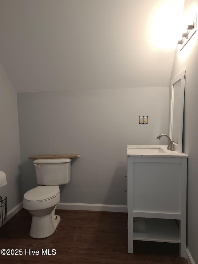 half bath with lofted ceiling, toilet, wood finished floors, and vanity