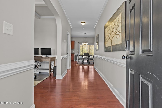 hall featuring a notable chandelier, arched walkways, crown molding, baseboards, and dark wood-style flooring