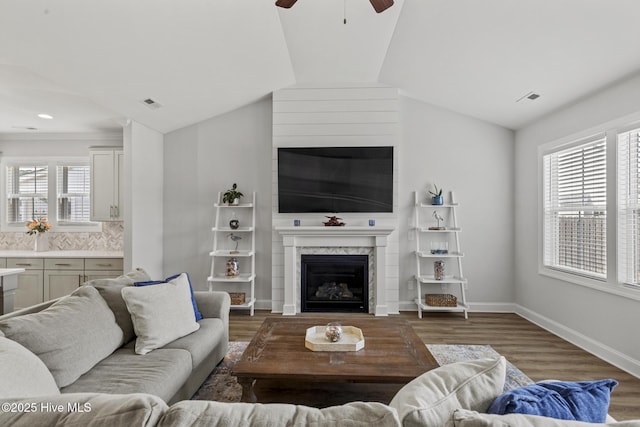 living area with wood finished floors, visible vents, a premium fireplace, ceiling fan, and vaulted ceiling