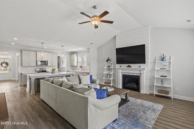 living room with dark wood-type flooring, baseboards, lofted ceiling, a premium fireplace, and a ceiling fan