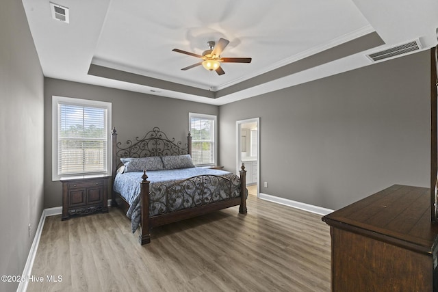 bedroom featuring a tray ceiling, visible vents, and wood finished floors