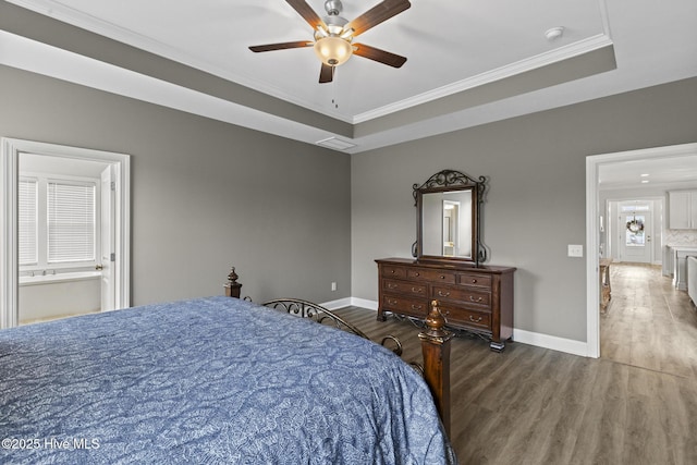 bedroom featuring a raised ceiling, wood finished floors, baseboards, and ornamental molding