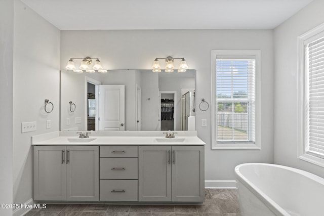 bathroom featuring double vanity, a freestanding tub, baseboards, and a sink