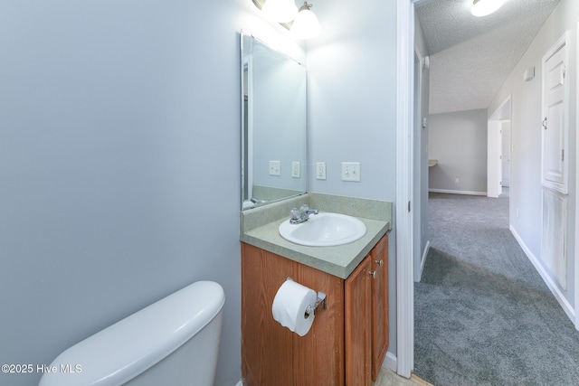 half bath featuring vanity, toilet, baseboards, and a textured ceiling