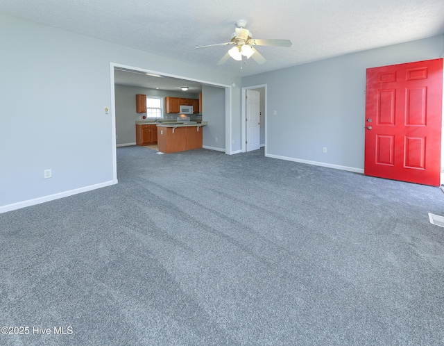 unfurnished living room with a textured ceiling, baseboards, a ceiling fan, and dark colored carpet