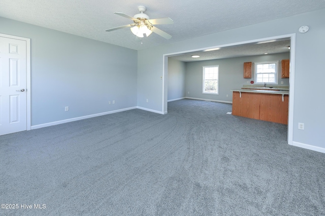 unfurnished living room featuring baseboards, dark carpet, a textured ceiling, and a ceiling fan