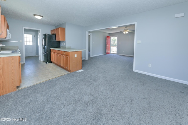 kitchen featuring white microwave, open floor plan, light countertops, freestanding refrigerator, and a ceiling fan