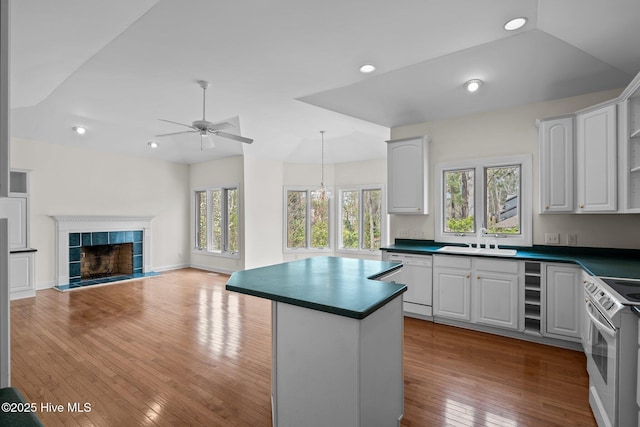 kitchen featuring a ceiling fan, a sink, dark countertops, white appliances, and wood-type flooring