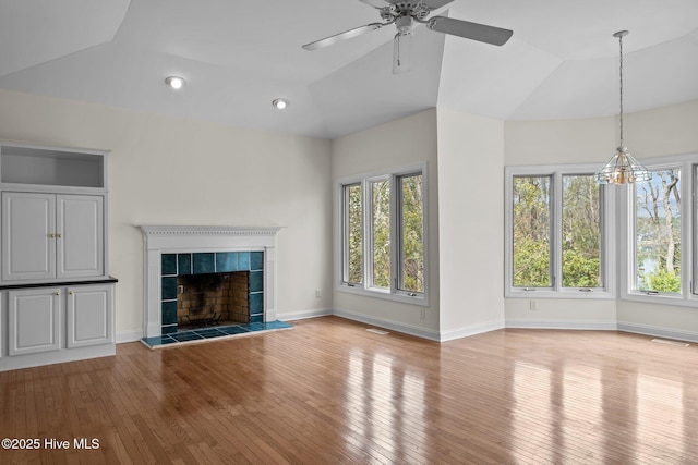 unfurnished living room with hardwood / wood-style floors, baseboards, ceiling fan, vaulted ceiling, and a tile fireplace