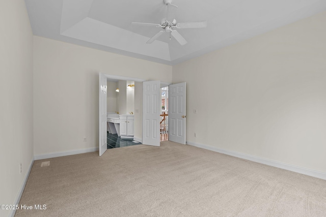 unfurnished bedroom featuring carpet flooring, ensuite bathroom, a raised ceiling, and baseboards