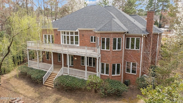 rear view of property featuring brick siding, stairway, roof with shingles, covered porch, and a chimney