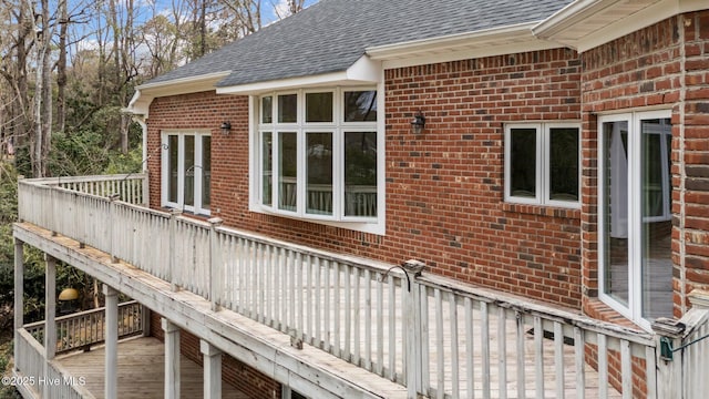 view of property exterior with brick siding, a wooden deck, and a shingled roof