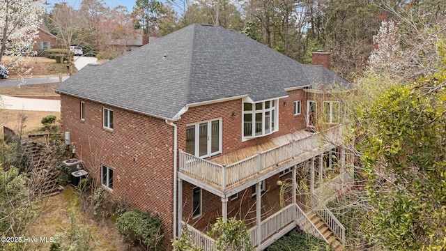 back of property with brick siding, a chimney, and a shingled roof