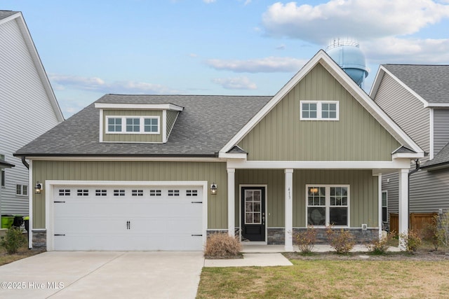 craftsman house with a shingled roof, covered porch, driveway, stone siding, and an attached garage