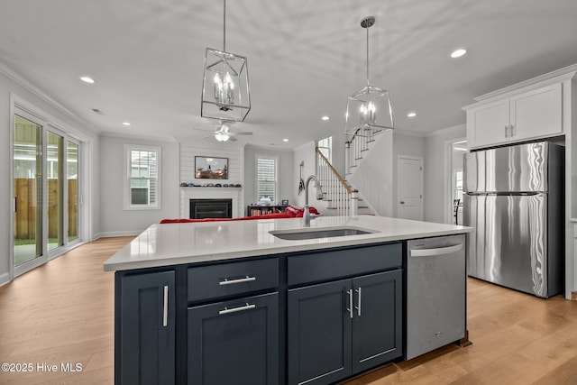 kitchen featuring a sink, light countertops, appliances with stainless steel finishes, crown molding, and open floor plan