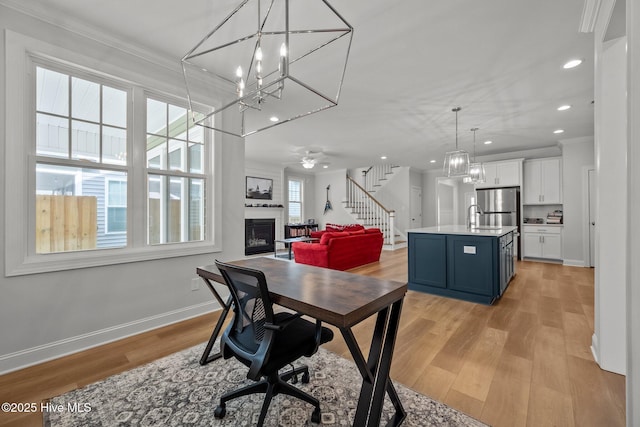 dining space featuring crown molding, baseboards, stairs, light wood-type flooring, and a glass covered fireplace