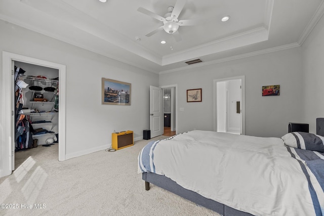 bedroom with carpet, visible vents, a tray ceiling, a walk in closet, and crown molding