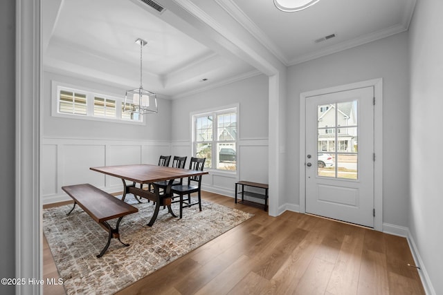 dining area featuring visible vents, wood-type flooring, crown molding, a raised ceiling, and a chandelier