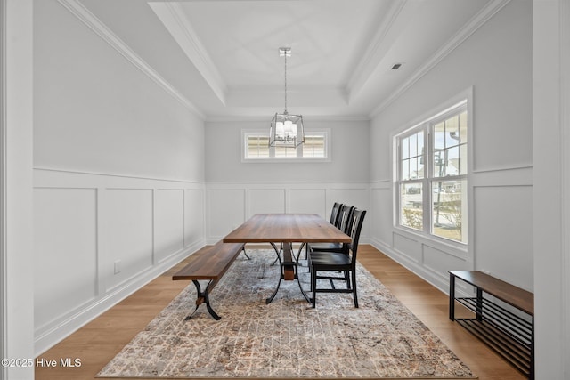 dining area featuring a tray ceiling, light wood-style flooring, a healthy amount of sunlight, and a chandelier