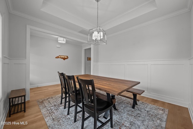 dining room featuring a tray ceiling, a notable chandelier, light wood-style flooring, and ornamental molding