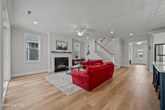 living room featuring visible vents, light wood-style flooring, stairs, and ornamental molding