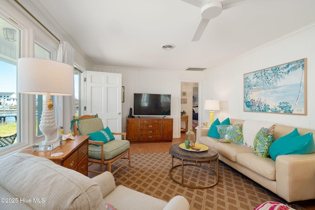 living room with visible vents, a ceiling fan, wood finished floors, and crown molding