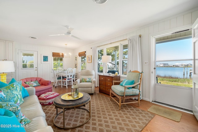 living room featuring ceiling fan, baseboards, a water view, and wood finished floors