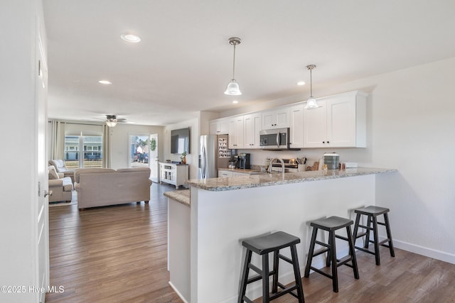 kitchen with appliances with stainless steel finishes, a breakfast bar, a peninsula, and wood finished floors