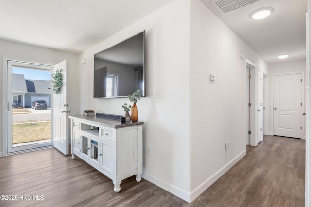 hall with a wealth of natural light, visible vents, baseboards, and wood finished floors