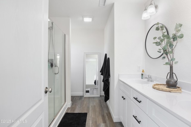 full bath with visible vents, a shower stall, double vanity, wood finished floors, and a sink