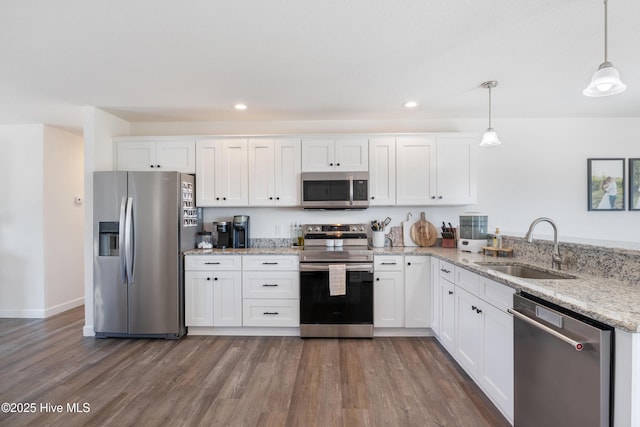 kitchen featuring pendant lighting, appliances with stainless steel finishes, wood finished floors, white cabinetry, and a sink