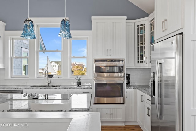 kitchen with a sink, glass insert cabinets, appliances with stainless steel finishes, white cabinetry, and backsplash