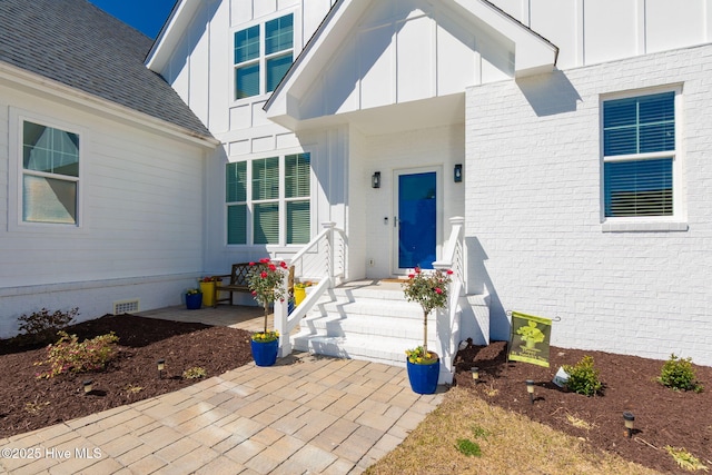 view of exterior entry featuring board and batten siding, roof with shingles, and crawl space