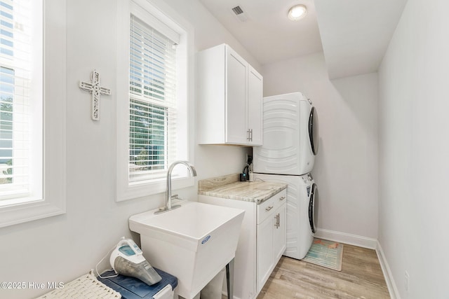 clothes washing area with visible vents, baseboards, stacked washer and dryer, cabinet space, and a sink