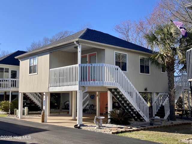 view of front of home featuring stairway, a carport, covered porch, and a shingled roof