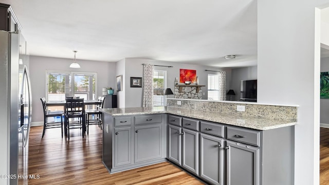 kitchen with light stone countertops, light wood-style flooring, stainless steel fridge with ice dispenser, gray cabinetry, and pendant lighting