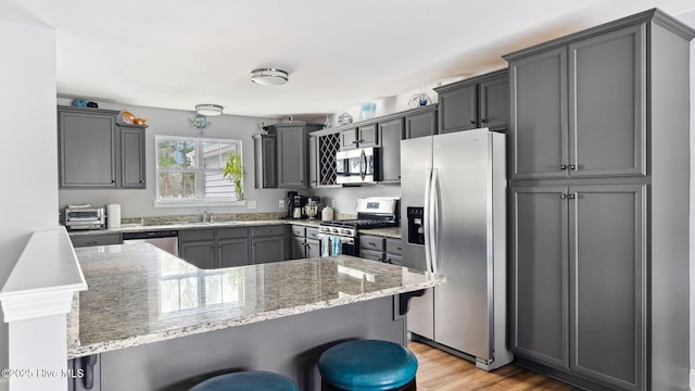 kitchen with a breakfast bar area, stainless steel appliances, light wood-type flooring, and light stone countertops