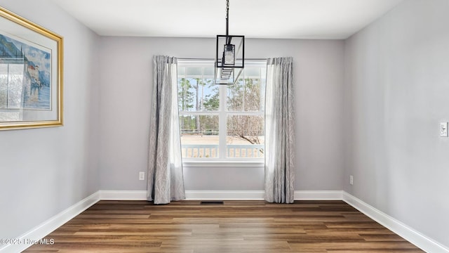 unfurnished dining area with baseboards, an inviting chandelier, and wood finished floors