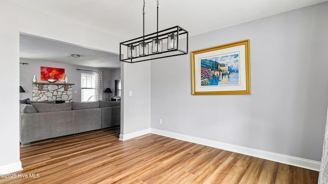 unfurnished living room featuring a stone fireplace, light wood-style flooring, and baseboards