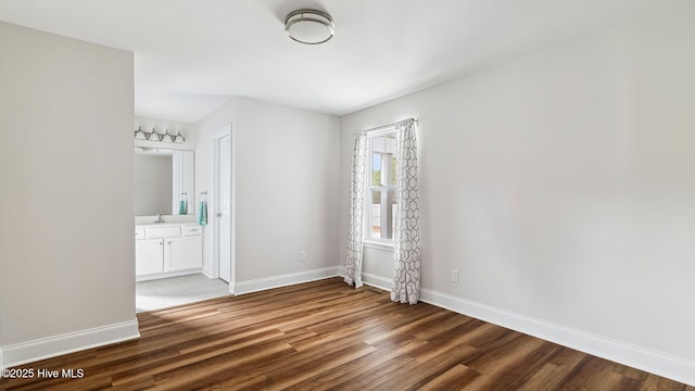 unfurnished bedroom featuring light wood-style flooring, connected bathroom, baseboards, and a sink