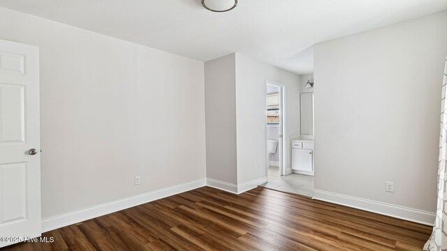 unfurnished bedroom featuring ensuite bath, wood finished floors, and baseboards