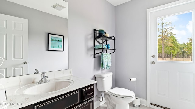 half bath with vanity, toilet, baseboards, and visible vents