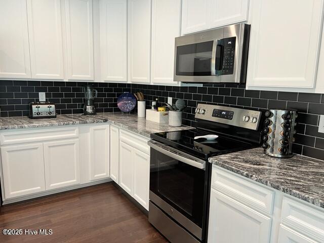 kitchen with stainless steel appliances, backsplash, white cabinets, and dark wood-style flooring