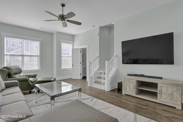 living room with ceiling fan, stairway, baseboards, and wood finished floors