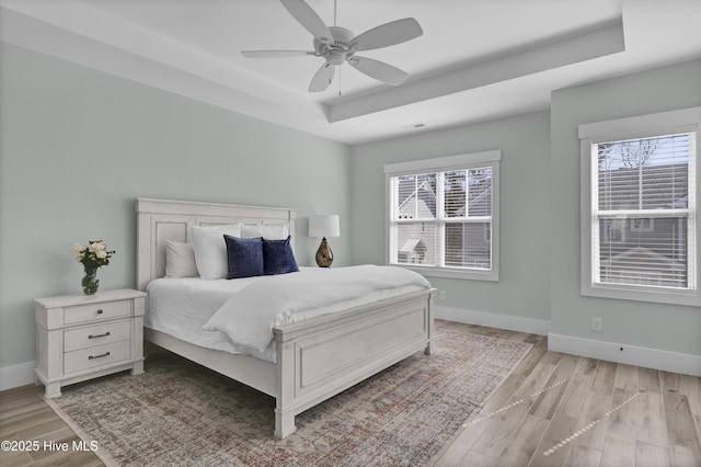 bedroom with a tray ceiling, multiple windows, and light wood-style floors