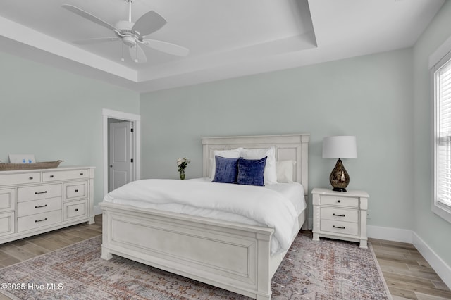 bedroom with baseboards, a tray ceiling, and wood finished floors