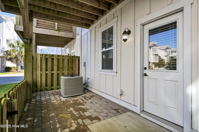 view of exterior entry featuring a patio, board and batten siding, central AC unit, and fence