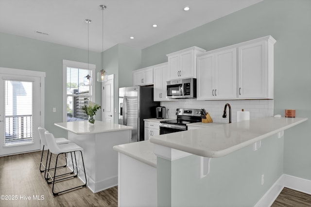 kitchen with a kitchen bar, backsplash, a center island, stainless steel appliances, and white cabinets