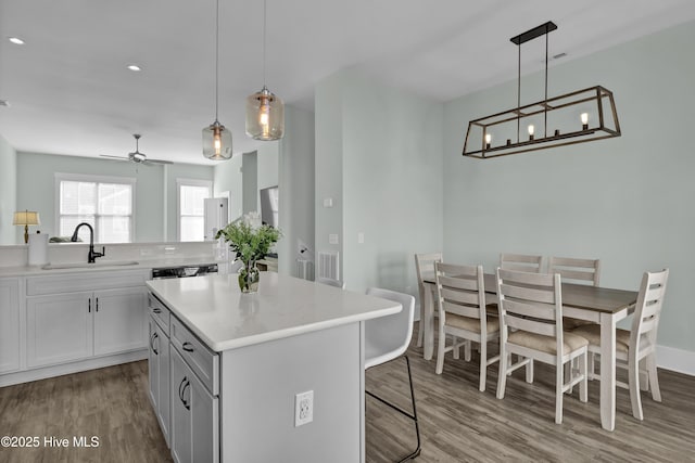 kitchen featuring a ceiling fan, a sink, wood finished floors, a center island, and a breakfast bar area