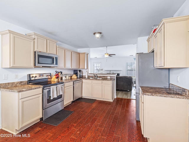 kitchen with dark wood finished floors, cream cabinetry, appliances with stainless steel finishes, and a peninsula